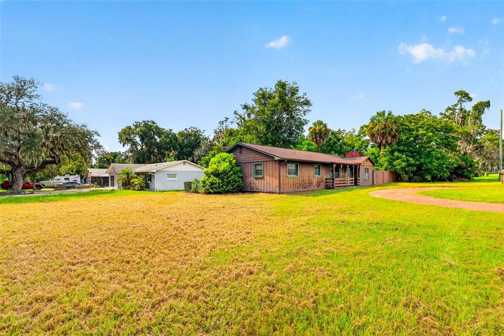 A brown wooden house sits on a large grassy lot next to a white building — 315 S LONE OAK DRIVE, LEESBURG, FL