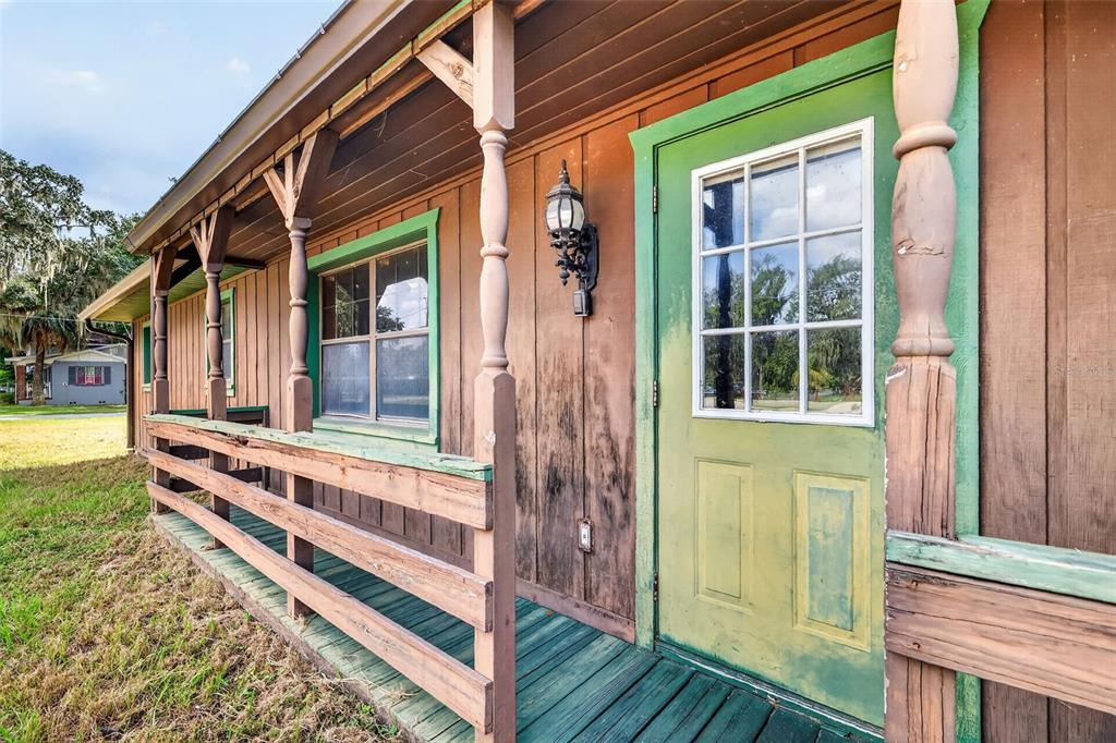 A wooden porch with a green door and railings runs along the side of a house — 315 S LONE OAK DRIVE, LEESBURG, FL