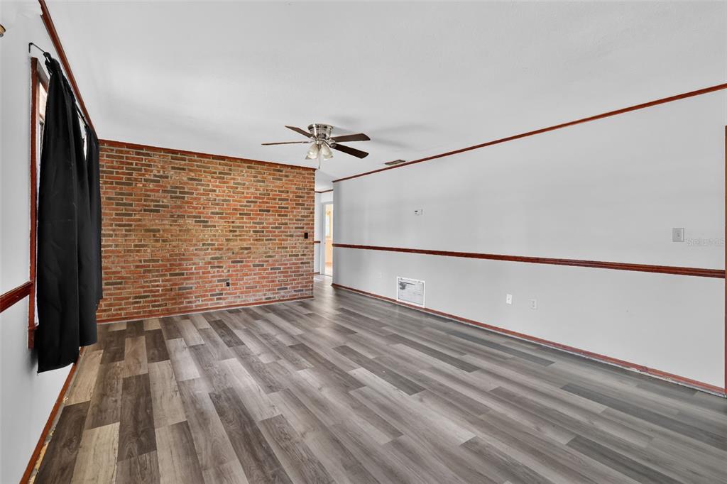 A living room features wood-look flooring, a brick accent wall, and a ceiling fan — 315 S LONE OAK DRIVE, LEESBURG, FL