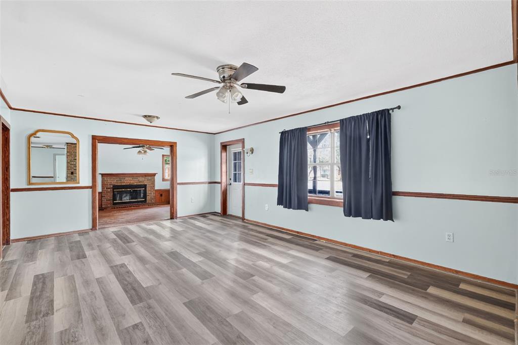 A living room with light blue walls, wood-look flooring, a ceiling fan, and a brick fireplace — 315 S LONE OAK DRIVE, LEESBURG, FL