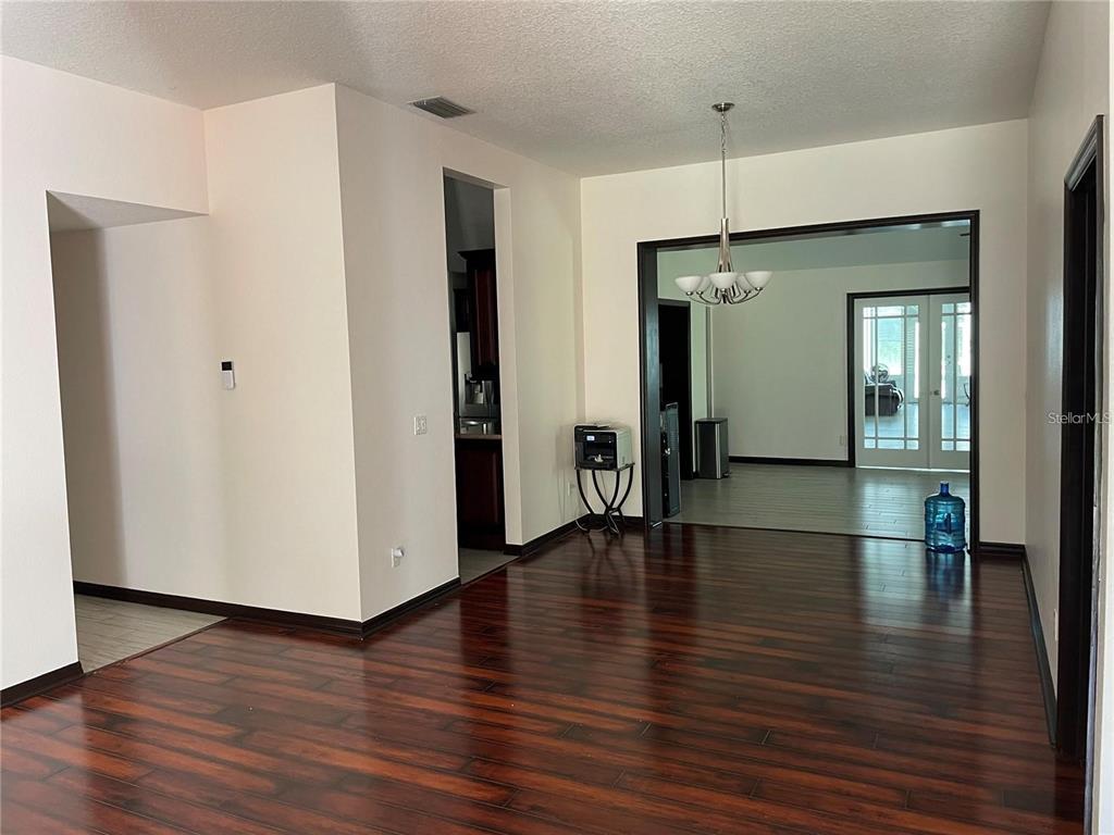 A dining room with dark hardwood floors leads into a living area with glass doors — 1858 N PRAIRIE DUNES COURT, OVIEDO, FL