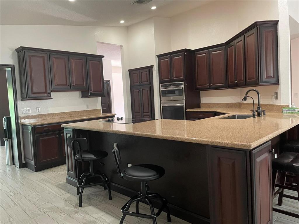 A kitchen features dark wood cabinets, granite countertops, a breakfast bar, and light tile flooring — 1858 N PRAIRIE DUNES COURT, OVIEDO, FL