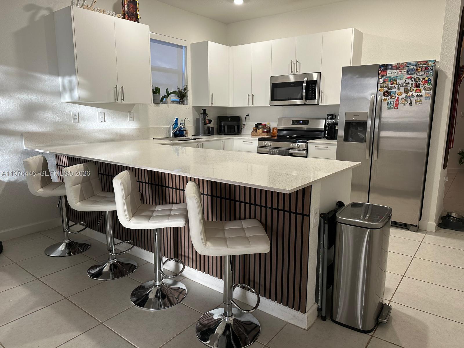 A kitchen features white cabinets, stainless steel appliances, a quartz countertop, and a slatted island — 18576 SW 136th Ct, Miami FL 33177, MIAMI, FL