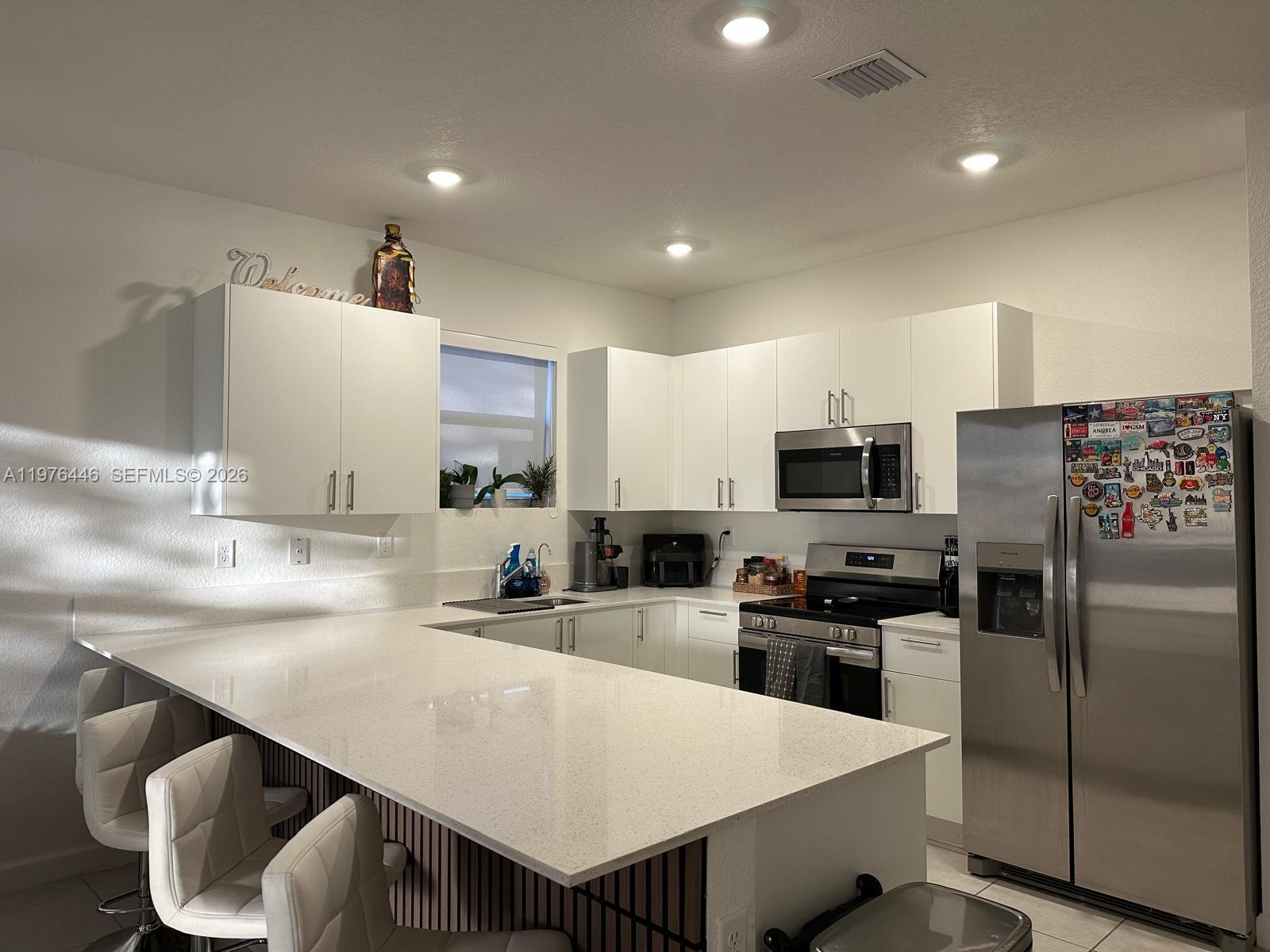 A modern kitchen features white cabinets, stainless steel appliances, and a large quartz-topped breakfast bar — 18576 SW 136th Ct, Miami FL 33177, MIAMI, FL