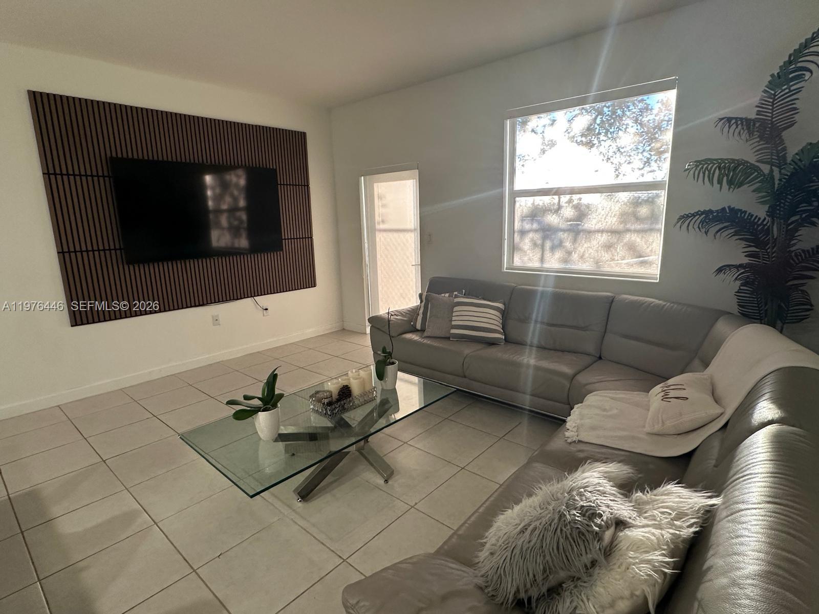 A living room features a gray sectional sofa, a glass coffee table, and a wood-slatted wall — 18576 SW 136th Ct, Miami FL 33177, MIAMI, FL