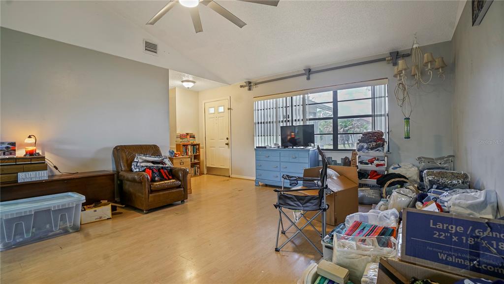 A living room with light wood flooring, a ceiling fan, and various boxes and furniture — 774 HARLAND COURT, KISSIMMEE, FL
