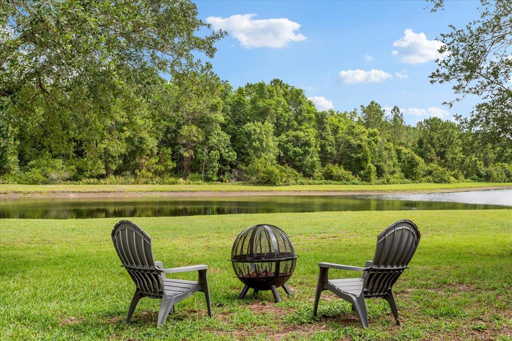 Two dark chairs and a metal fire pit sit on a grassy lawn by water — 9997 CHARDONNAY DRIVE, ORLANDO, FL