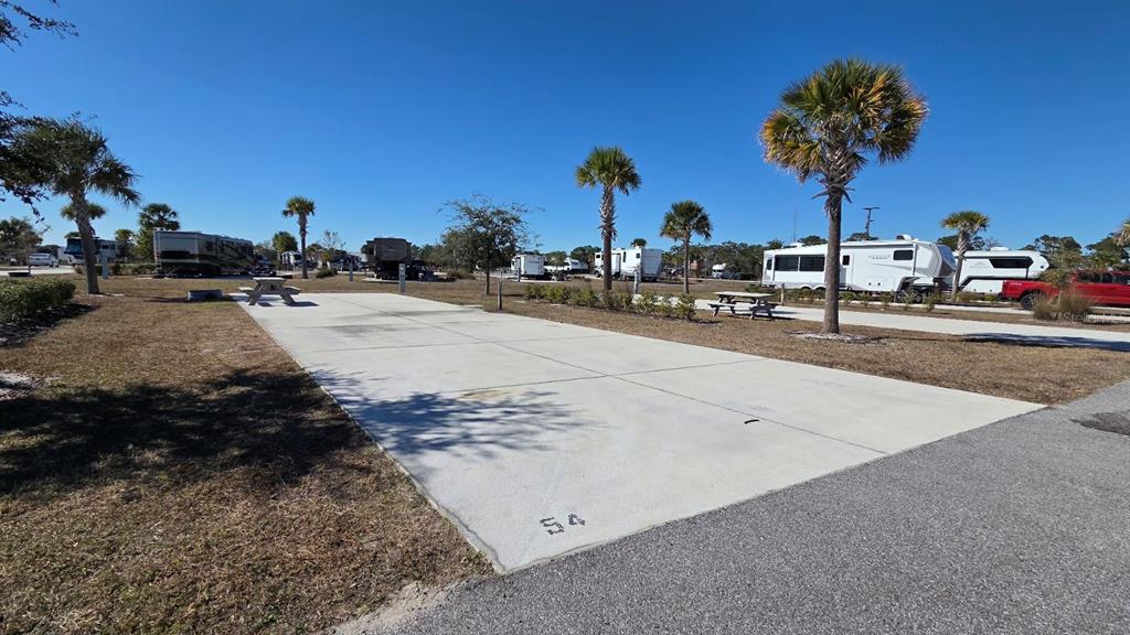 A concrete RV campsite pad numbered 54 is surrounded by grass and palm trees — 54 TIKI TURN E, LAKE WALES, FL