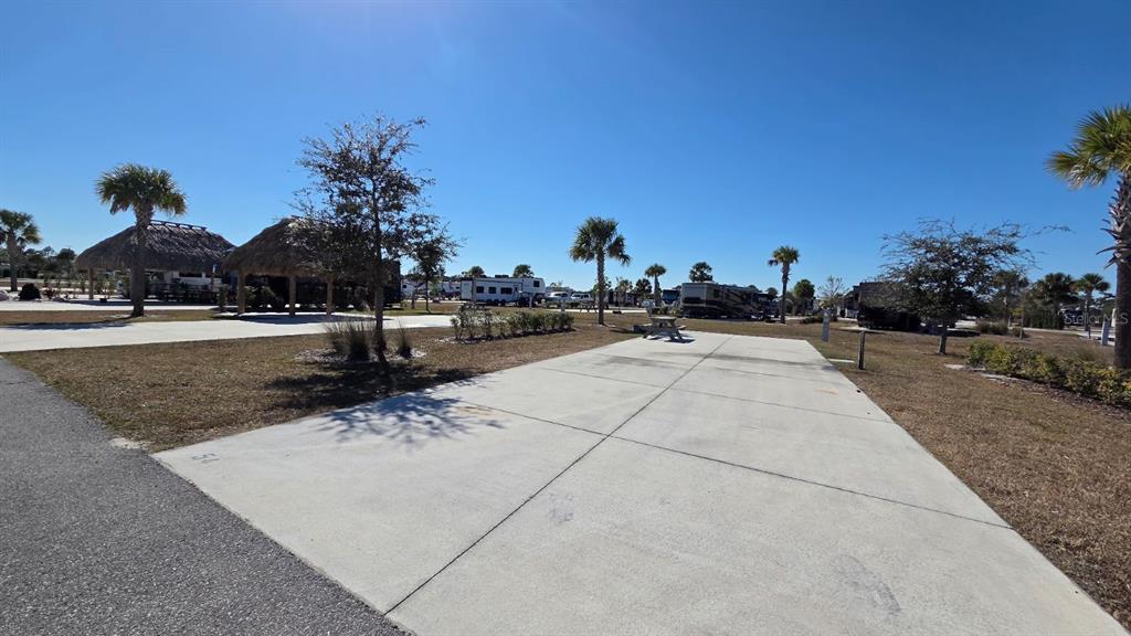 A concrete RV pad sits in a sunny outdoor campground with palm trees and structures — 54 TIKI TURN E, LAKE WALES, FL