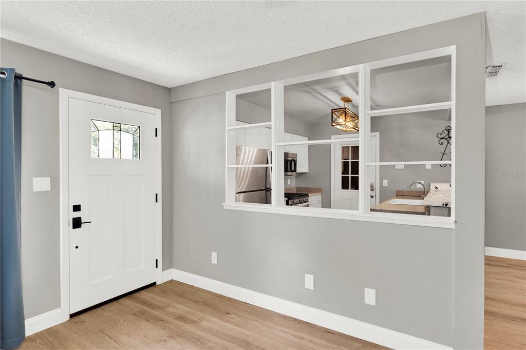 A room with light wood flooring, gray walls, a white door, and a kitchen pass-through window — 5556 MEMORIAL DRIVE, ORLANDO, FL