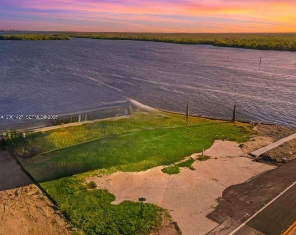 An aerial view shows a vacant waterfront lot with a paved road and sunset sky — 4767 Pine Island RD NW, Matlacha FL 33993, MATLACHA, FL