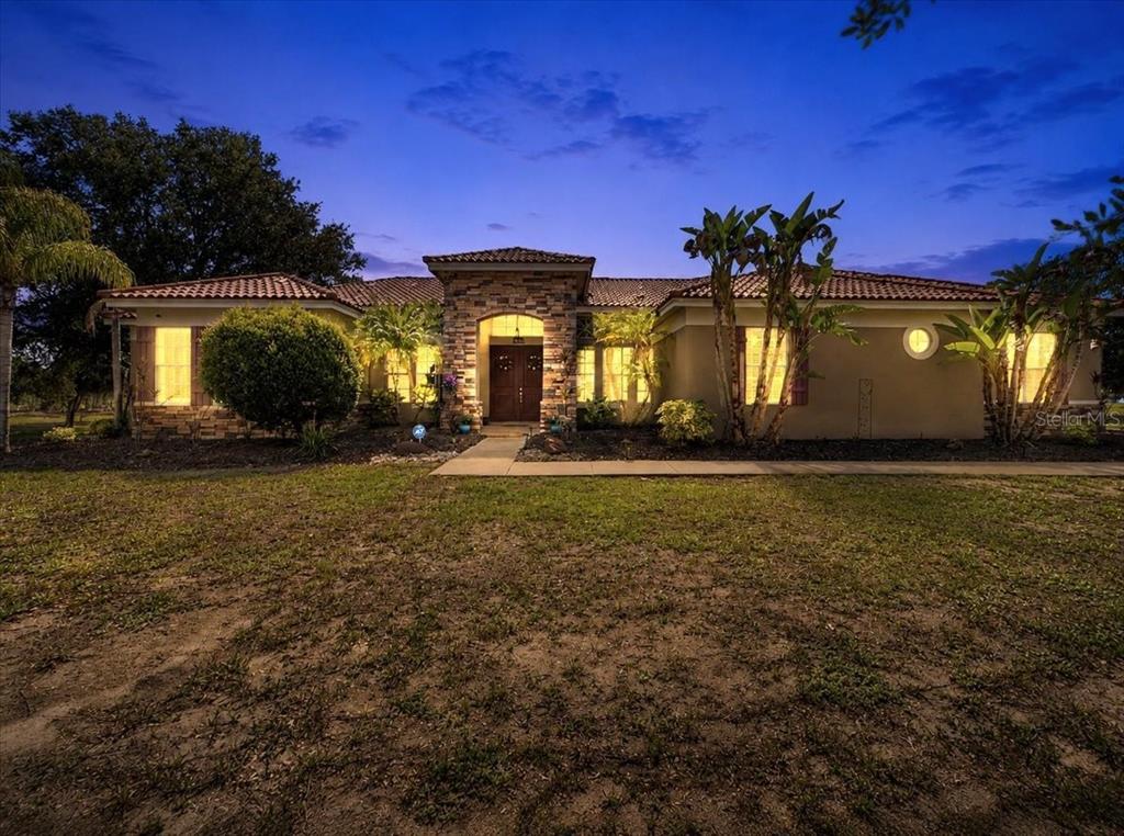 A single-story house with a stone-accented entryway and a tile roof at dusk — 5325 LAKE SIENA DRIVE, WIMAUMA, FL