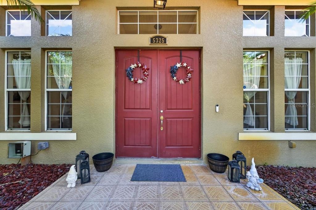 A red double front door with wreaths sits on a tiled porch with two gnomes — 5325 LAKE SIENA DRIVE, WIMAUMA, FL