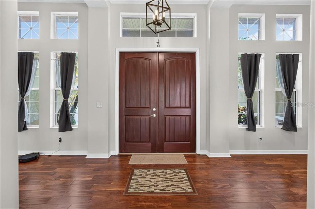 A foyer features dark wood floors, a double front door, and tall windows with curtains — 5325 LAKE SIENA DRIVE, WIMAUMA, FL