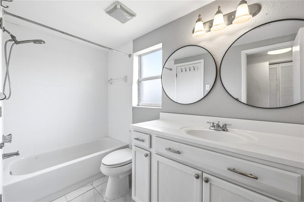 A bathroom features a white vanity with two round mirrors, a toilet, and a tub-shower — 7328 MAKO DRIVE, HUDSON, FL
