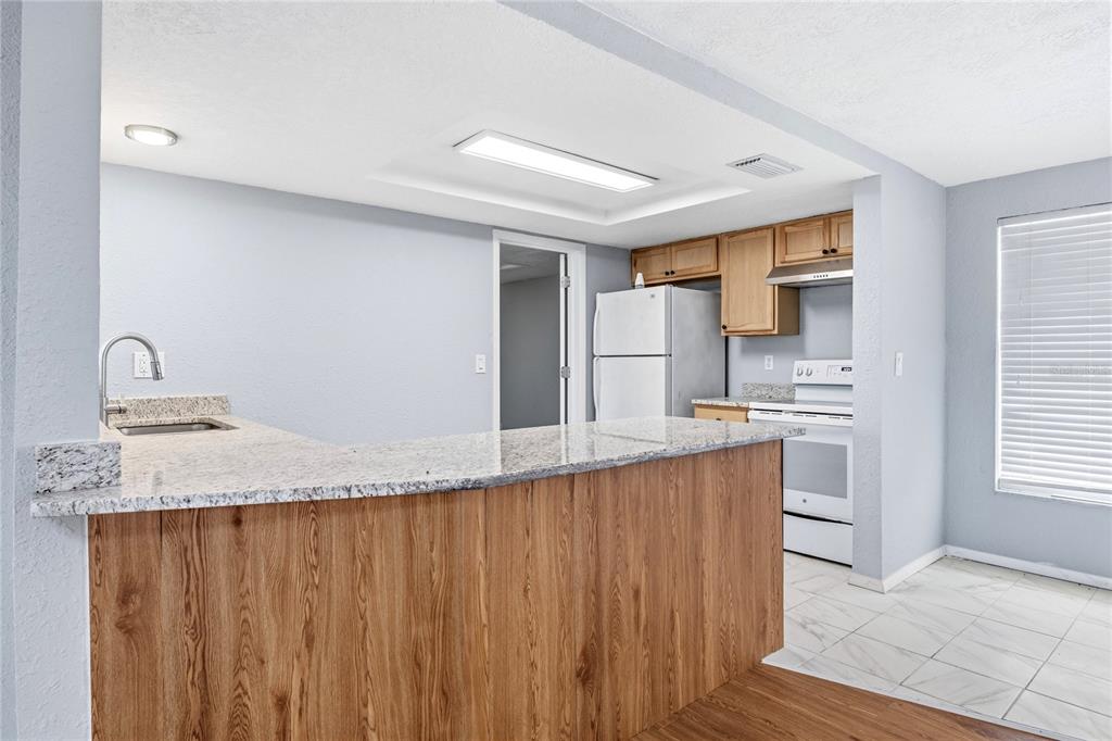 A kitchen features a wood-paneled breakfast bar, granite countertops, white appliances, and light blue walls — 7328 MAKO DRIVE, HUDSON, FL