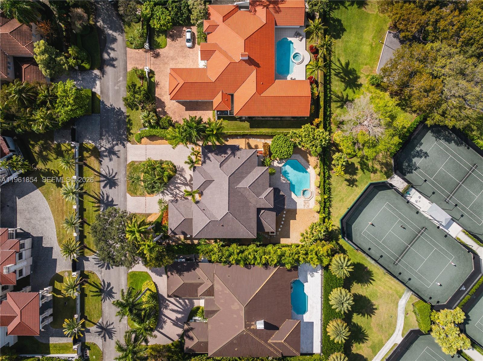 An aerial view shows three houses with pools and two tennis courts in a neighborhood — 129 Gavilan Ave, Coral Gables FL 33143, CORAL GABLES, FL