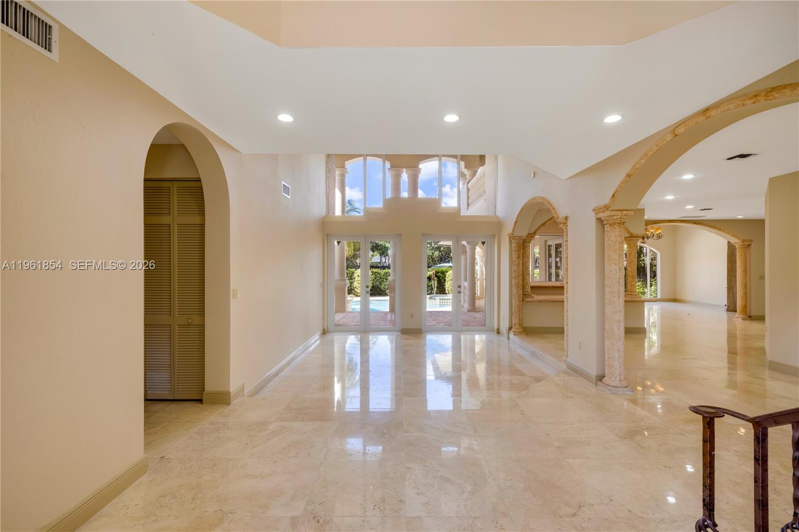 A spacious, light-filled foyer features polished stone floors, arched entryways, and tall glass doors — 129 Gavilan Ave, Coral Gables FL 33143, CORAL GABLES, FL