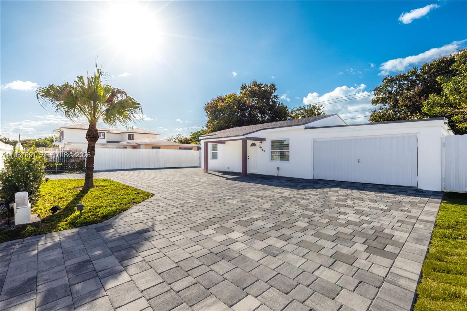 A white single-story house features a large paved driveway and a palm tree — 10050 SW 171st St # 10050, Miami FL 33157, MIAMI, FL