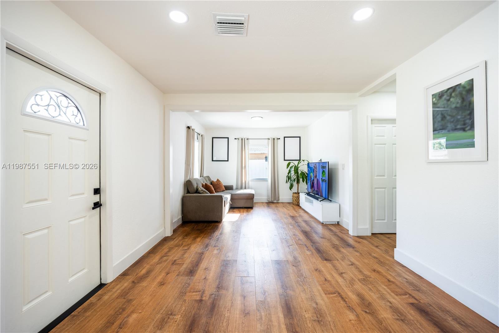 A living room features wood-look flooring, white walls, and a sectional sofa near a window — 10050 SW 171st St # 10050, Miami FL 33157, MIAMI, FL