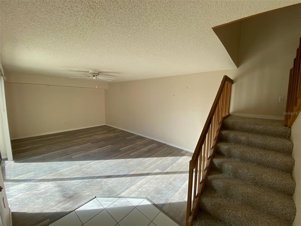 An empty living room features wood-look flooring, a ceiling fan, and carpeted stairs — 2911 PECAN AVENUE, LEESBURG, FL