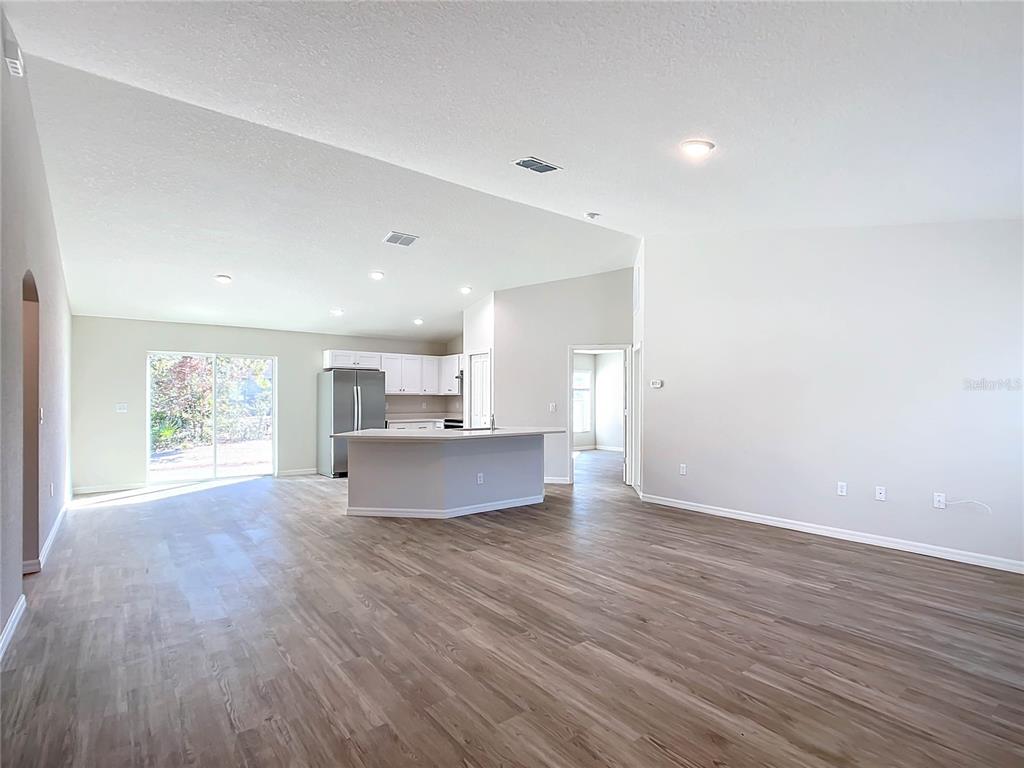 An open-concept living area features light wood-look flooring, white walls, and a kitchen island — 4810 SW 139TH STREET ROAD, OCALA, FL