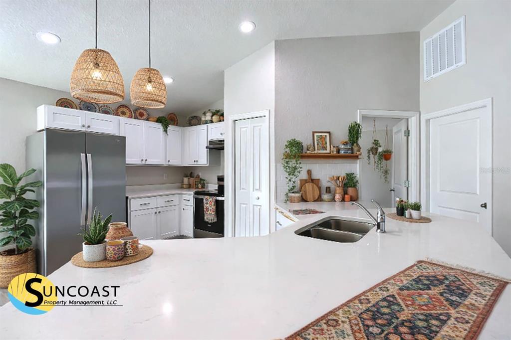A kitchen features white cabinetry, stainless steel appliances, a quartz island, and woven pendant lights — 4810 SW 139TH STREET ROAD, OCALA, FL