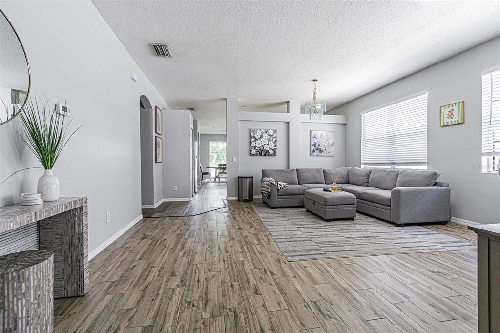 A living room features gray wood-look tile flooring, a sectional sofa, and neutral walls — 13016 TERRACE BROOK PLACE, TEMPLE TERRACE, FL