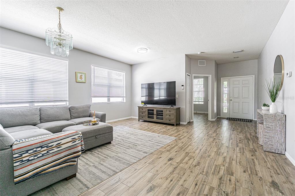 A living room features a grey sectional sofa, wood-look flooring, and a television on a console — 13016 TERRACE BROOK PLACE, TEMPLE TERRACE, FL