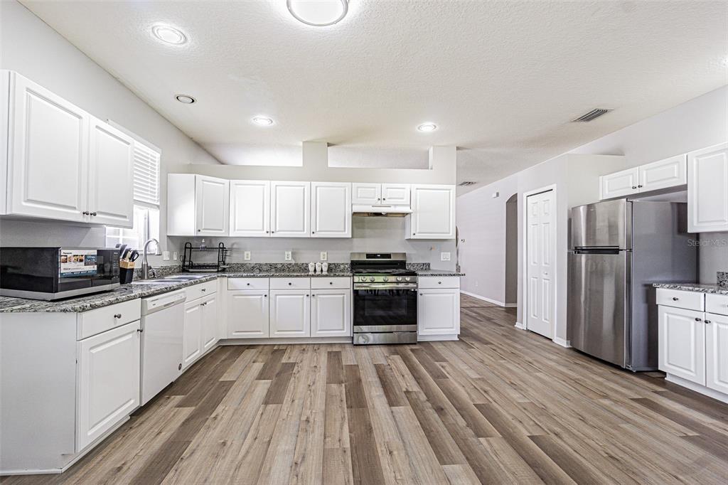 A kitchen with white cabinets, stainless steel appliances, granite countertops, and wood-look flooring — 13016 TERRACE BROOK PLACE, TEMPLE TERRACE, FL