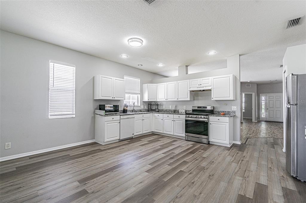 A kitchen features white cabinets, granite countertops, stainless steel appliances, and wood-look flooring — 13016 TERRACE BROOK PLACE, TEMPLE TERRACE, FL