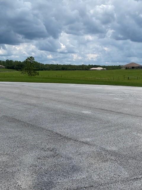 A paved area sits in the foreground before a large, grassy field under cloudy skies — 5698 QUICKSILVER, FLORAL CITY, FL