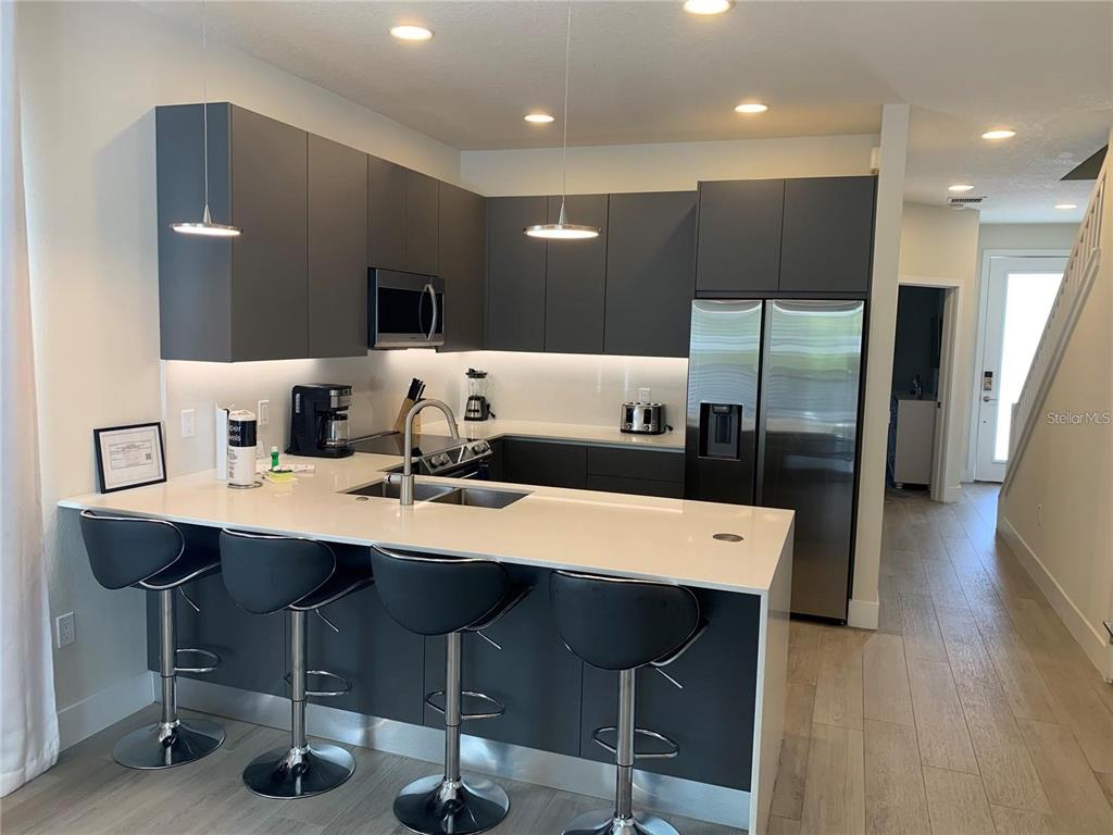 A modern kitchen features dark gray cabinetry, stainless steel appliances, and a white breakfast bar — 17307 HIDDEN FOREST DRIVE, CLERMONT, FL
