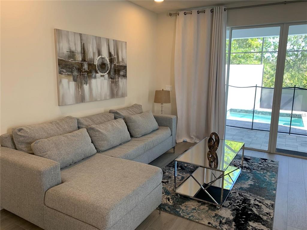 A living room with a gray sectional sofa, mirrored coffee table, and sliding door to pool — 17307 HIDDEN FOREST DRIVE, CLERMONT, FL