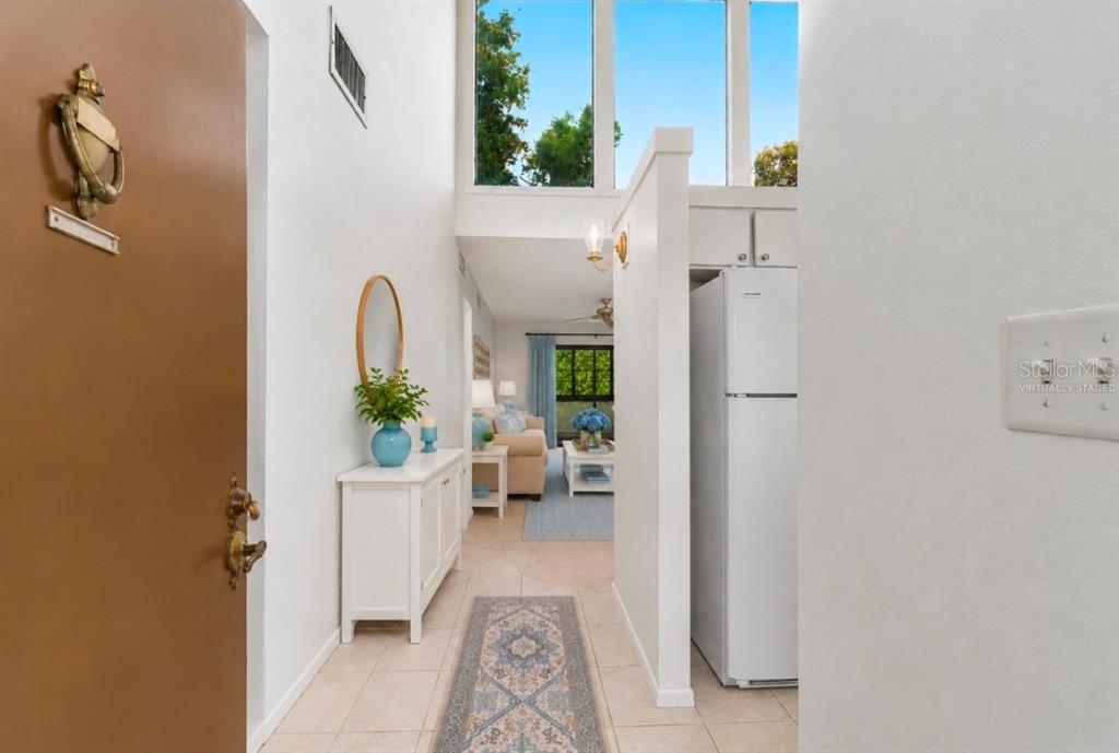 An entryway leads past a white cabinet and refrigerator into a living room with high windows — 2415 NE 7TH STREET UNIT 8, OCALA, FL
