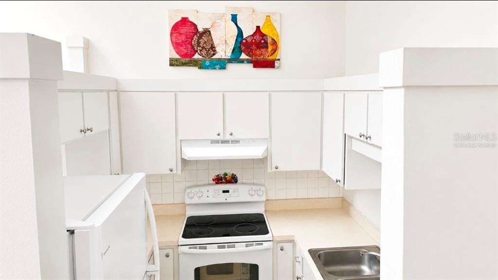 A small kitchen features white cabinets, a white electric stove, and a stainless steel sink — 2415 NE 7TH STREET UNIT 8, OCALA, FL