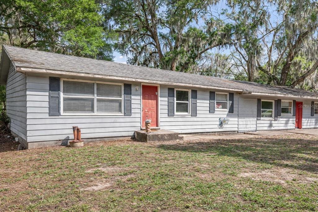 A single-story house with gray siding, a red front door, and dark shutters at dusk — 4849 GRAND AVENUE, DE LEON SPRINGS, FL
