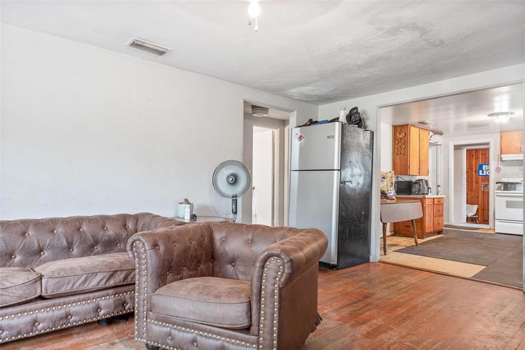 A living room with a brown tufted sofa and chair leads into a kitchen area — 4849 GRAND AVENUE, DE LEON SPRINGS, FL