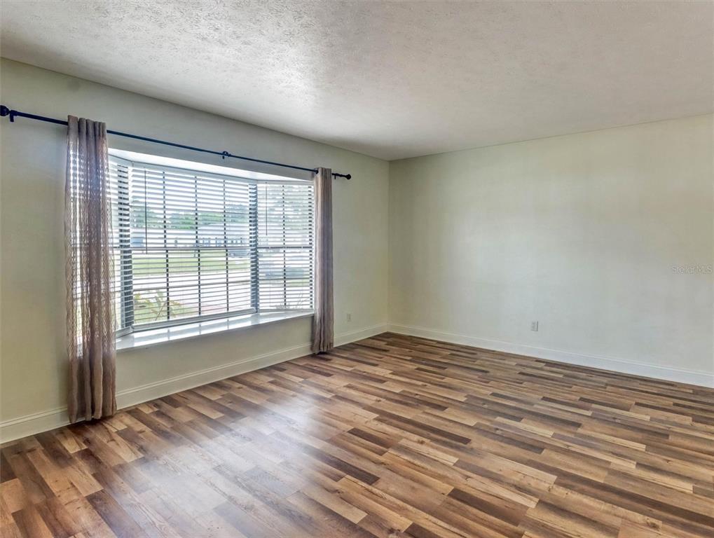 An empty room features wood-look flooring, a large bay window with blinds, and light-colored walls — 13346 MORAN DRIVE, TAMPA, FL