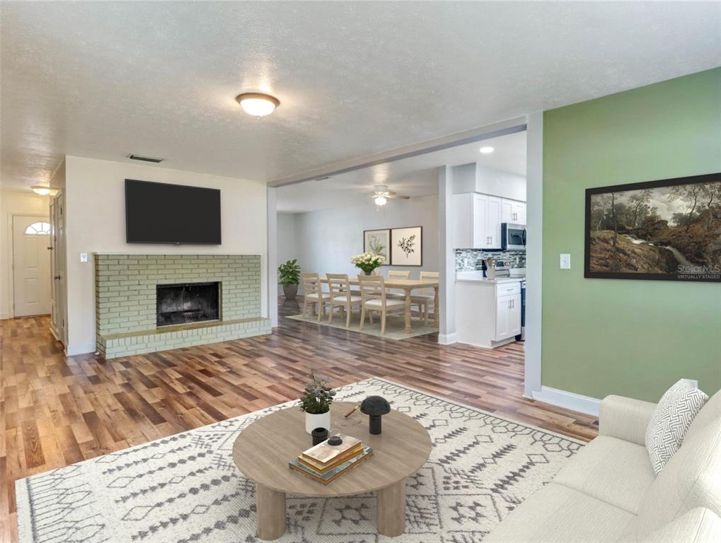 A living room with a brick fireplace, wood flooring, and an adjacent dining area — 13346 MORAN DRIVE, TAMPA, FL