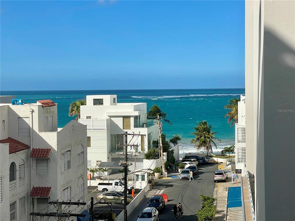 An elevated view of a coastal street with white buildings, parked cars, and the ocean — 1124 ASHFORD AVENUE UNIT 6A, SAN JUAN, PR