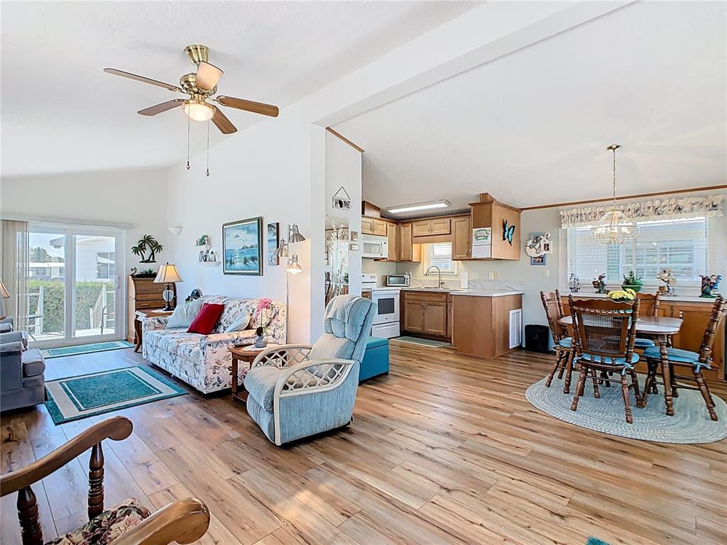 An open-concept living room and kitchen area features wood-look flooring and a vaulted ceiling — 9000 US HWY 192 UNIT 311, CLERMONT, FL