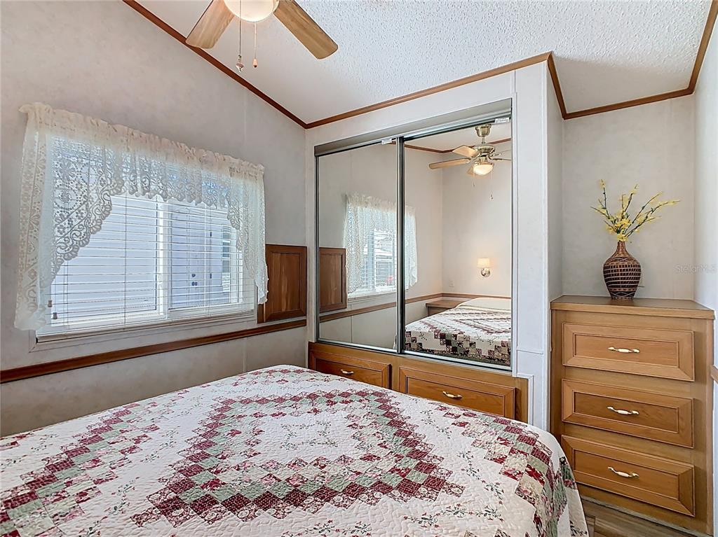 A bedroom features a bed with a quilt, mirrored closet doors, and a wooden dresser — 9000 US HWY 192 UNIT 311, CLERMONT, FL