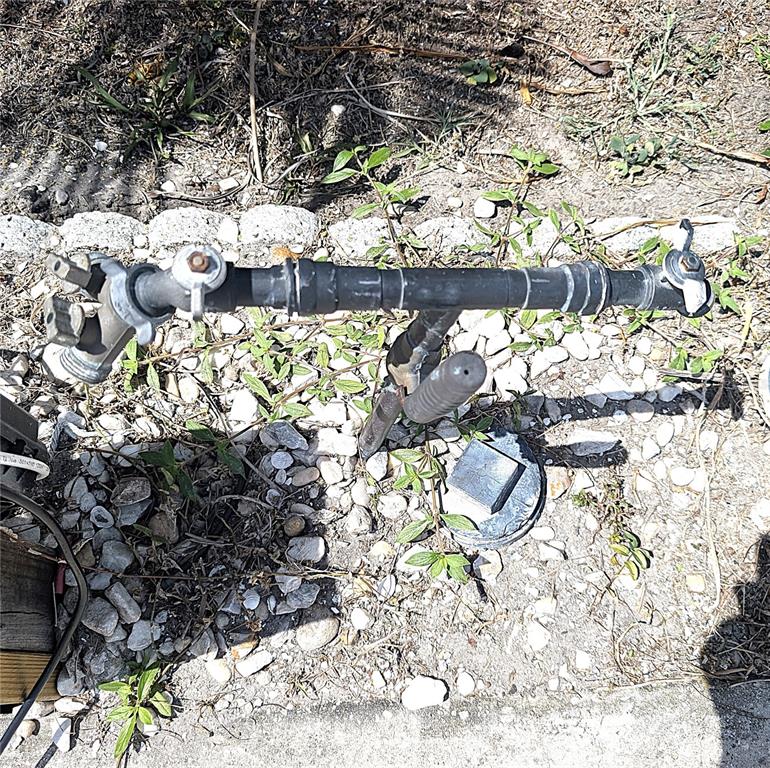 An outdoor water pipe assembly with two spigots stands above a small utility access cover — 3333 26TH AVENUE E UNIT 1335, BRADENTON, FL
