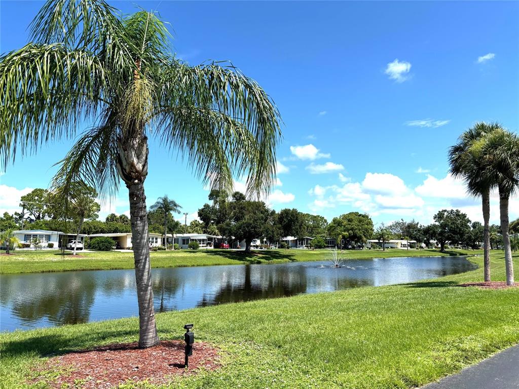 A pond with a fountain is surrounded by palm trees and mobile homes under a sky — 239 ESTRADA, NORTH PORT, FL