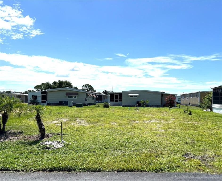 A grassy lot sits in front of several single-story manufactured homes under a blue sky — 239 ESTRADA, NORTH PORT, FL