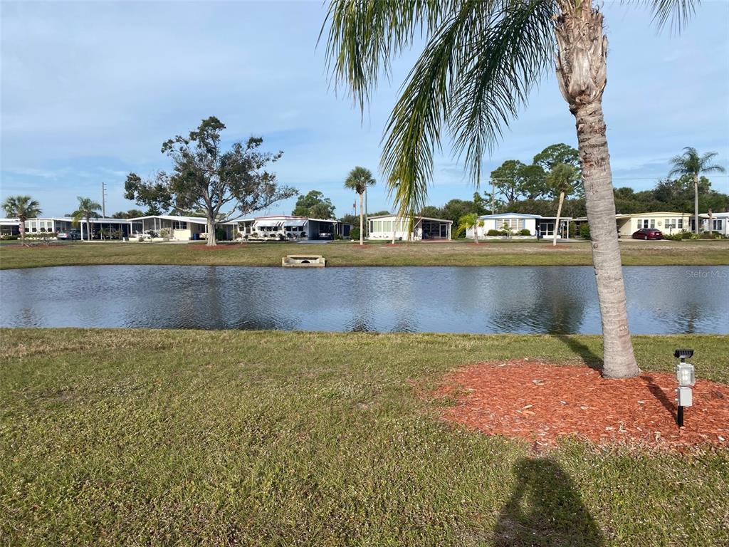 A pond sits in front of several manufactured homes under a clear blue sky — 239 ESTRADA, NORTH PORT, FL