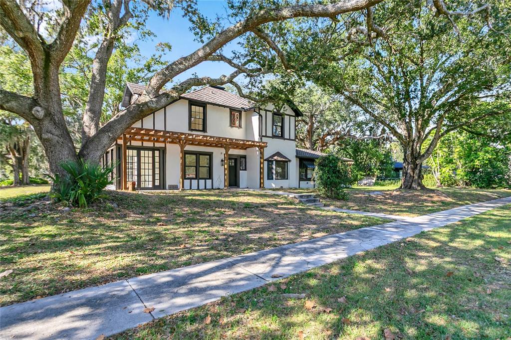 A two-story Tudor-style house with a wooden pergola stands among large oak trees — 226 N ELLIOTT AVENUE, SANFORD, FL