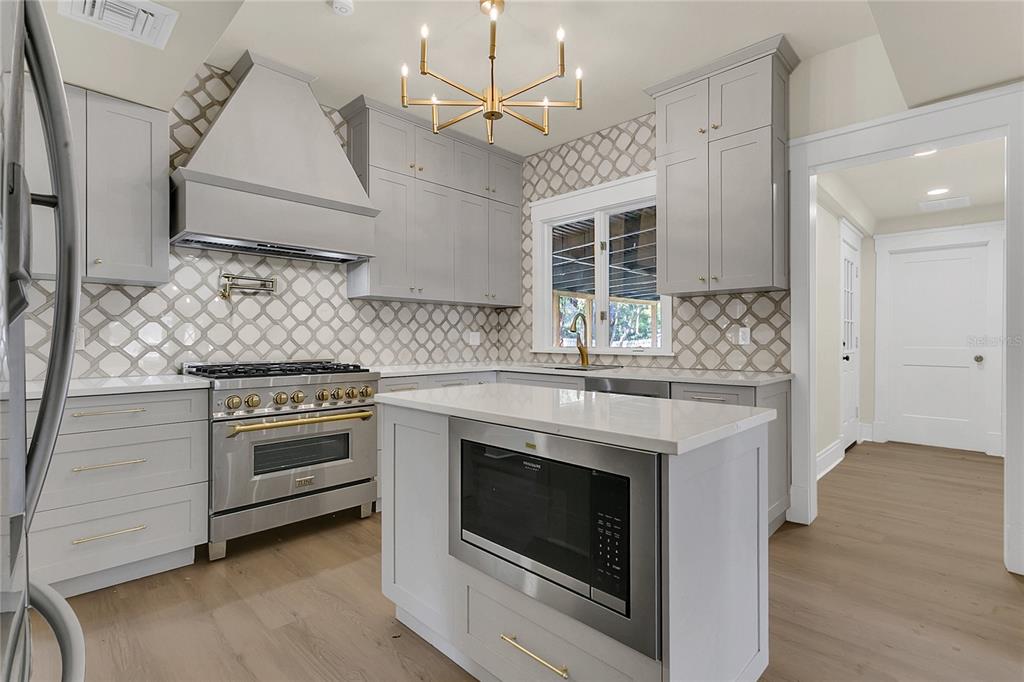 A kitchen features gray cabinets, a white tile backsplash, a stainless steel range, and an island — 226 N ELLIOTT AVENUE, SANFORD, FL