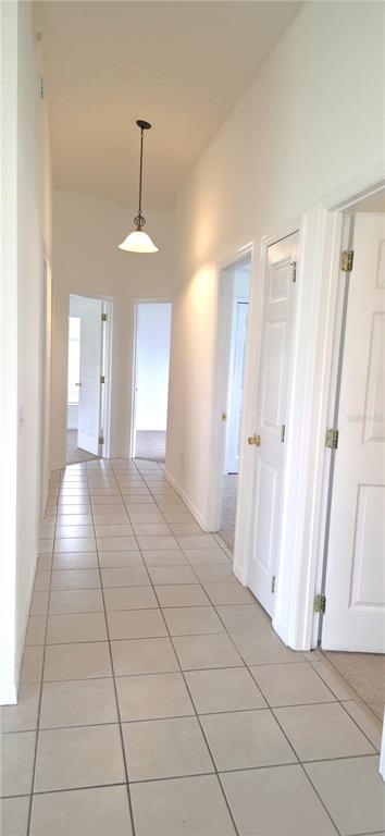 A hallway with beige tile flooring features a hanging pendant light and several white doors — 2160 EOLA COURT, OVIEDO, FL